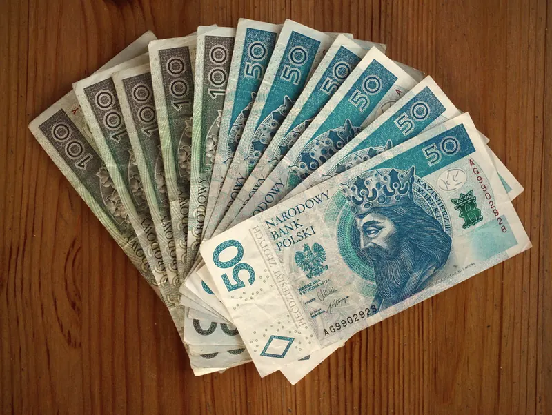 Banknoty 50 i 100 złotych rozłożone na drewnianym blacie